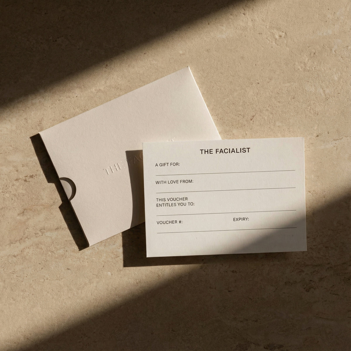 A Facialist gift card and envelope on stone, in late afternoon light