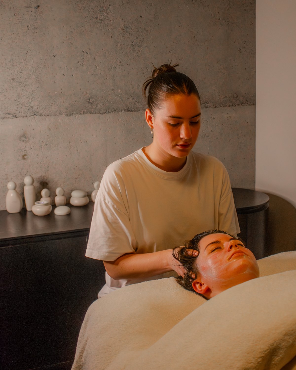 A facialist at the head of the bed, looking at the skin before a facial